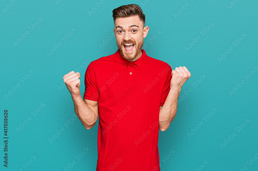 Young redhead man wearing casual clothes celebrating surprised and amazed for success with arms raised and open eyes. winner concept. Young redhead man wearing casual clothes celebrating surprised and amazed for success with arms raised and open eyes. winner concept.