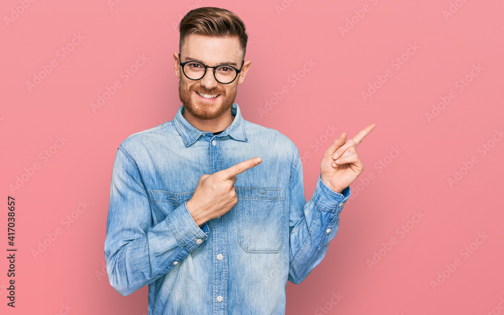 Young redhead man wearing casual denim shirt smiling and looking at the camera pointing with two hands and fingers to the side. Young redhead man wearing casual denim shirt smiling and looking at the camera pointing with two hands and fingers to the side.
