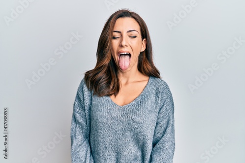 Young brunette woman wearing casual winter sweater sticking tongue out happy with funny expression. emotion concept.