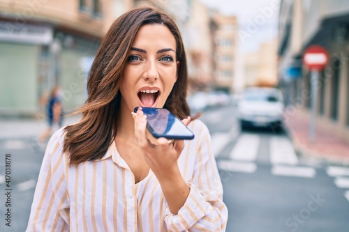 Wallpaper Mural Young hispanic woman smiling happy sending voice message using smartphone at the city. Torontodigital.ca