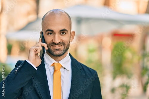 Young hispanic bald businessman smiling happy talking on the smartphone at the city.