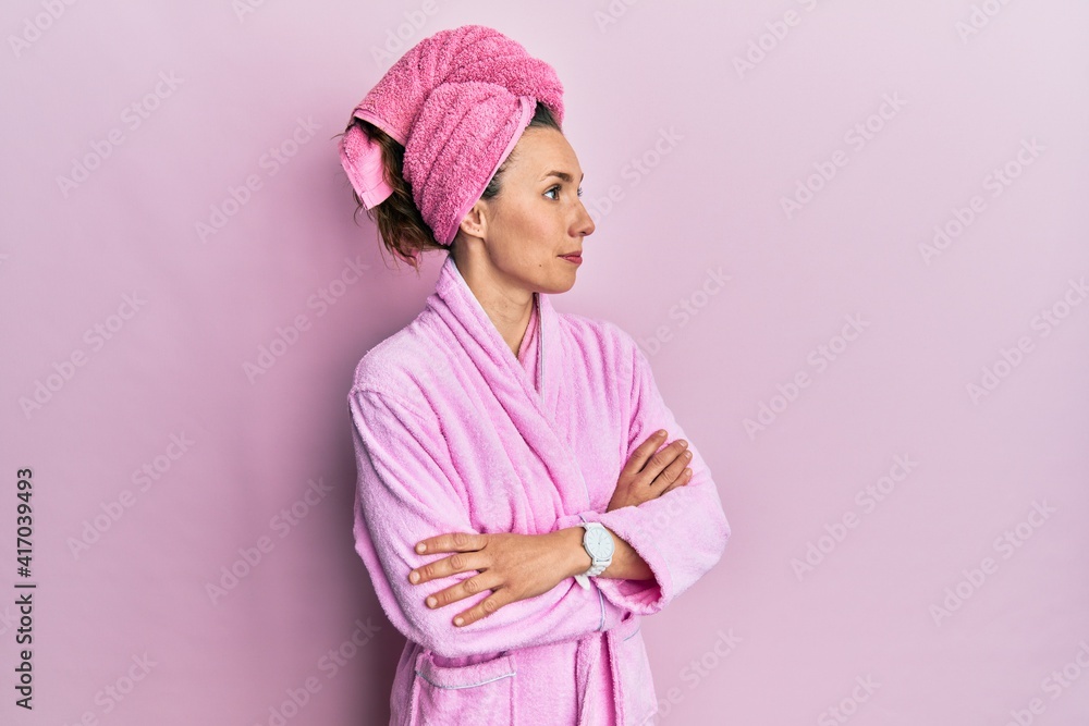 Young blonde woman wearing shower towel cap and bathrobe looking to the side with arms crossed convinced and confident Young blonde woman wearing shower towel cap and bathrobe looking to the side with arms crossed convinced and confident