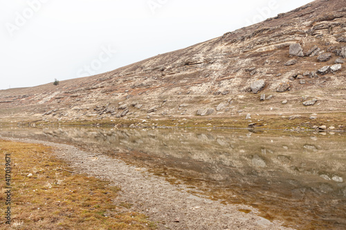 Hill with rocks reflected in the water . Scenery of Stone Age