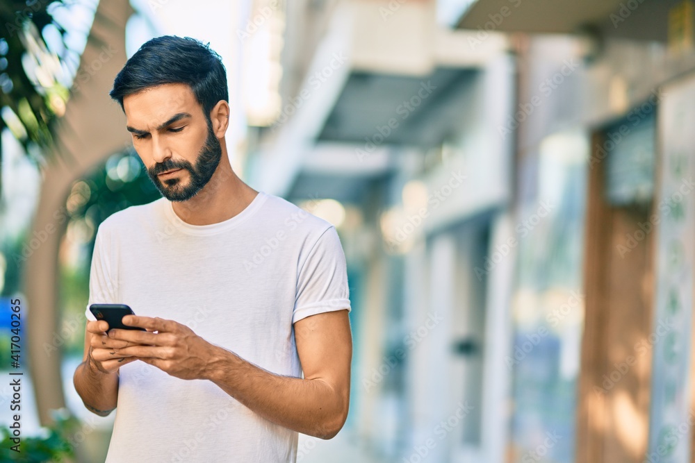 Young hispanic man with serious expression using smartphone at the city. Young hispanic man with serious expression using smartphone at the city.