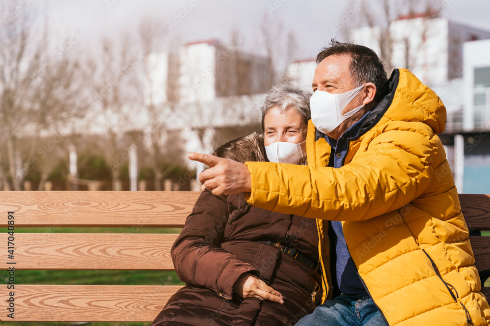 Lovely senior couple in medical masks relaxing on a bench in the park Lovely senior couple in medical masks relaxing on a bench in the park