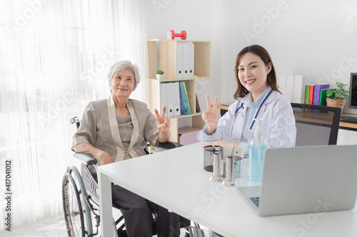 asian female doctor and old patient show v sign with hands in hospital, they talk about healthcare promotion and disease screening, elderly health check up