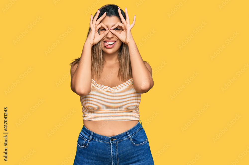 Beautiful brunette woman wearing casual clothes doing ok gesture like binoculars sticking tongue out, eyes looking through fingers. crazy expression. Beautiful brunette woman wearing casual clothes doing ok gesture like binoculars sticking tongue out, eyes looking through fingers. crazy expression.