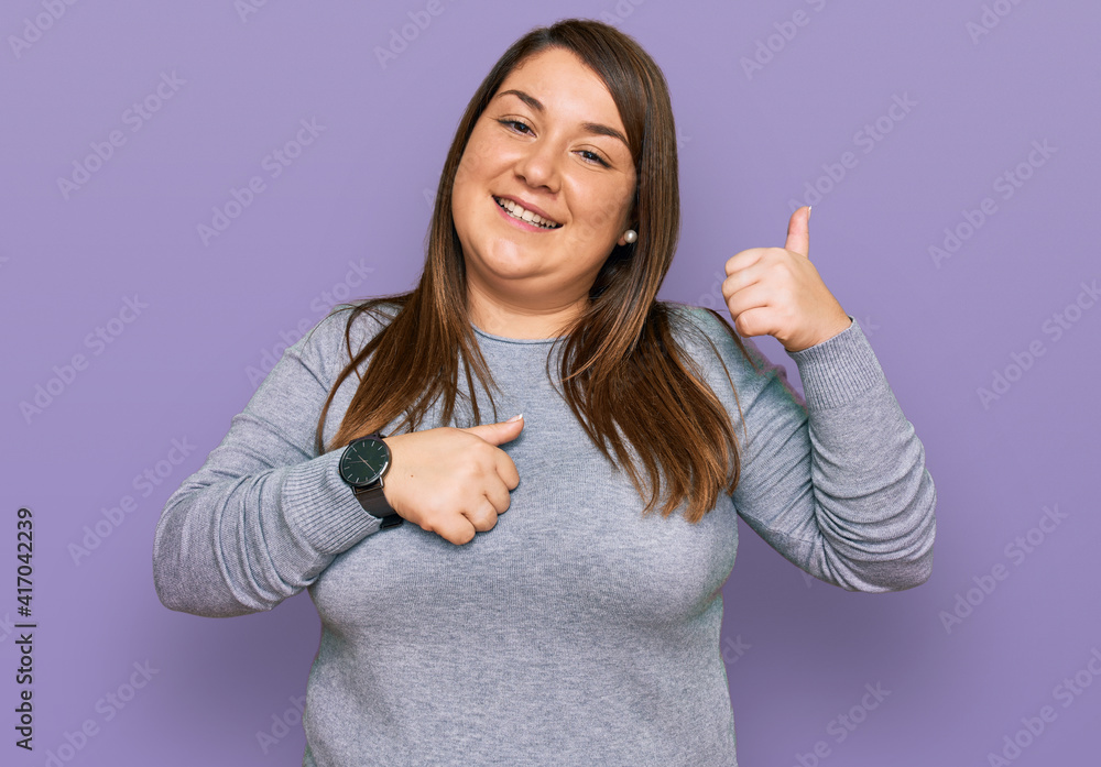 Beautiful brunette plus size woman wearing casual clothes pointing to the back behind with hand and thumbs up, smiling confident Beautiful brunette plus size woman wearing casual clothes pointing to the back behind with hand and thumbs up, smiling confident
