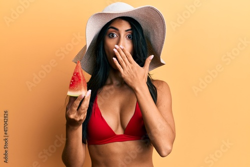 Beautiful hispanic woman wearing bikini eating watermelon covering mouth with hand  shocked and afraid for mistake. surprised expression