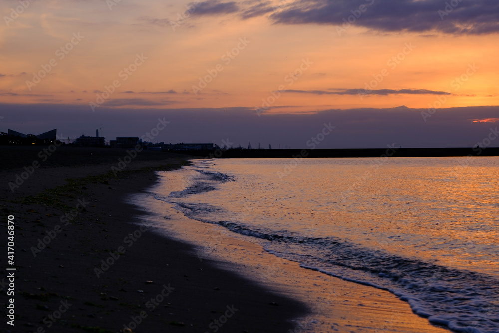 神戸、須磨浦海岸の夜明け。日が昇り、空と雲、砂浜と波がオレンジ色に染まる。