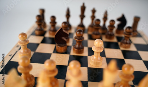 White and black wooden pieces on a chessboard. A chessboard set up during a game on a gray background.