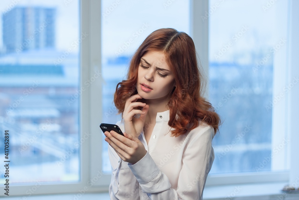 Fototapeta premium cheerful red-haired woman with a phone in her hands communicating an official office