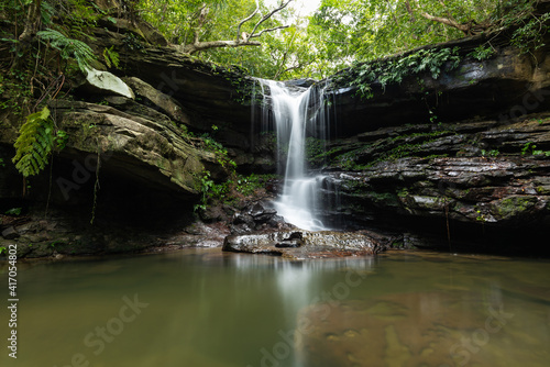 Serene scene of the Kuura waterfall reflected in a river pool surrounded by rocks in the middle of the jungle. Iriomote Island.