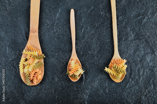 Various uncooked pasta on wooden spoons over dark background