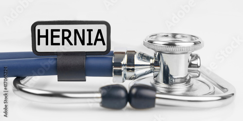 On the white surface lies a stethoscope with a plate with the inscription - HERNIA