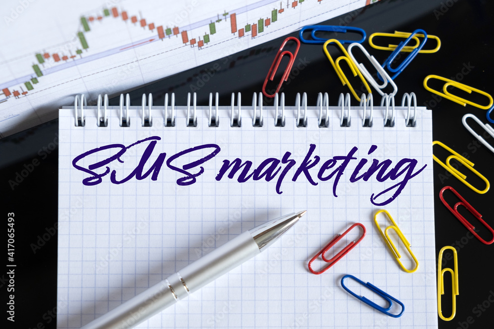 On the desktop are a forex chart, paper clips, a pen and a notebook in which it is written - SMS marketing On the desktop are a forex chart, paper clips, a pen and a notebook in which it is written - SMS marketing