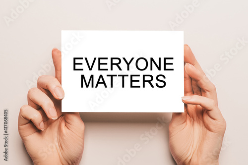 Female hands hold card paper with text Everyone Matters on a yellow background. Business and finance concept