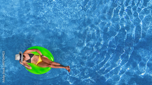 Beautiful woman in hat in swimming pool aerial view from above, young girl relaxes and has fun on inflatable ring in water on vacation 
