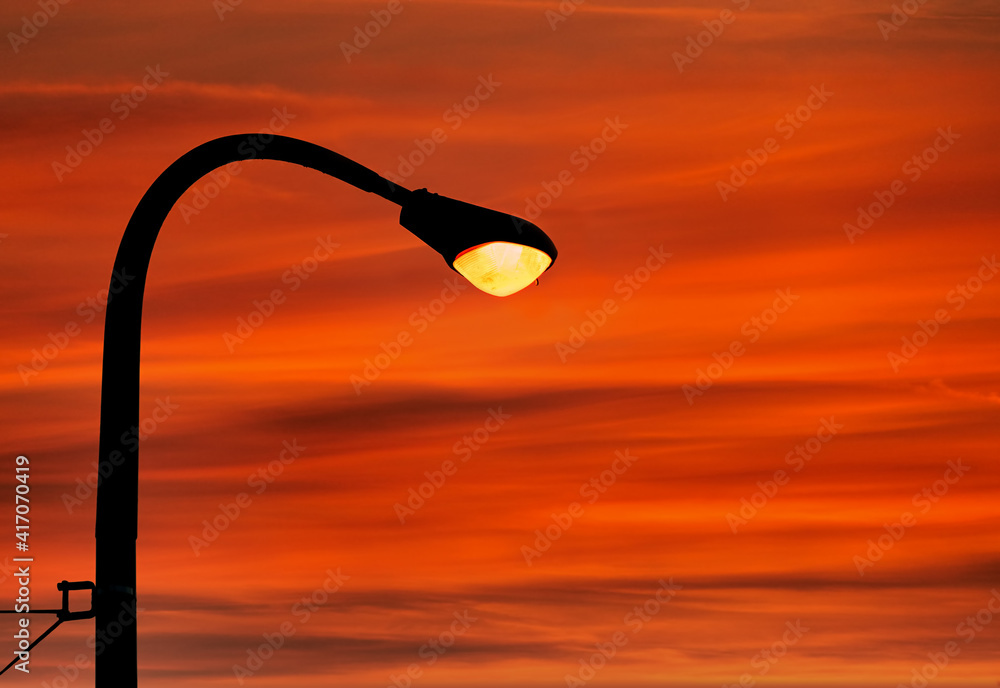Illuminated street light and pole against red cloudy sunset sky background Illuminated street light and pole against red cloudy sunset sky background
