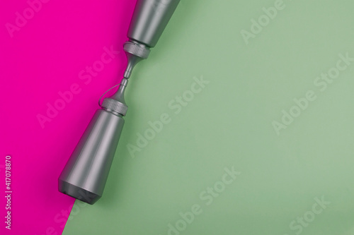 Two gray plastic bottles on a pink and green background.