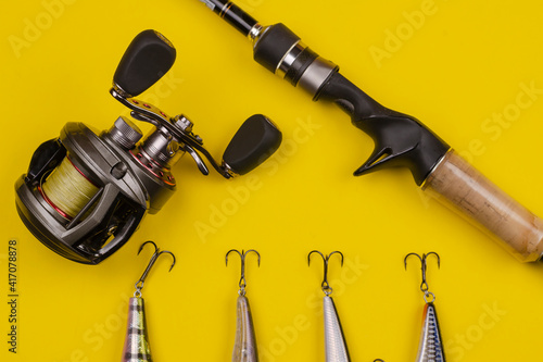 Fishing rod baitcasting reel and baits on a yellow background.
