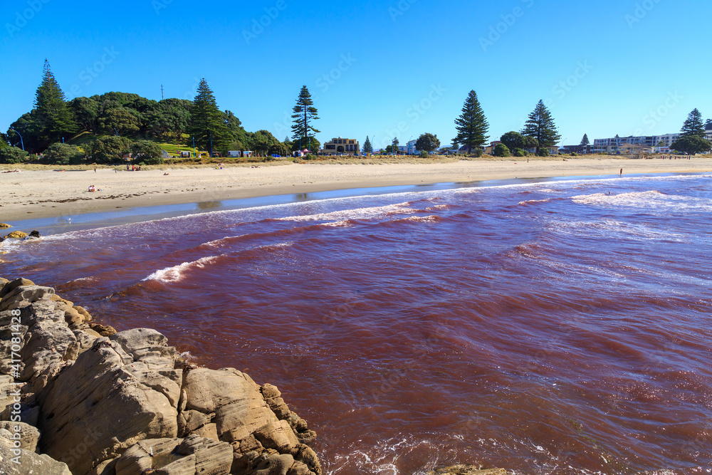 A "red tide" washing ashore at Mount Maunganui, New Zealand. This is an algal bloom caused by a storm pushing up nutrients from the seabed - obrazy, fototapety, plakaty 