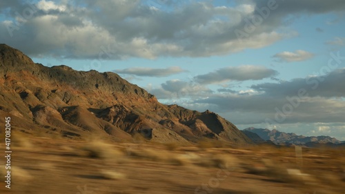 Fototapeta Naklejka Na Ścianę i Meble -  Road trip, driving auto from Death Valley to Las Vegas, Nevada USA. Hitchhiking traveling in America. Highway journey, dramatic atmosphere, sunset mountain and Mojave desert wilderness. View from car.