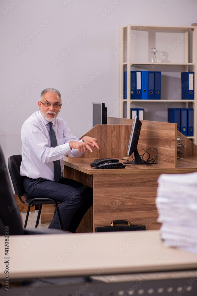 Old male employee unhappy with excessive work in the office Old male employee unhappy with excessive work in the office