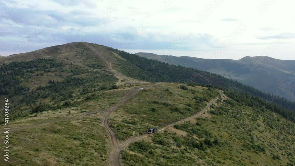 Aerial view off-road vehicle with a trailer driving on a mountain road. drone flight video Aerial view off-road vehicle with a trailer driving on a mountain road. drone flight video