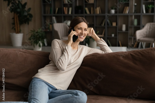 Happy millennial Caucasian woman sit relax on sofa at home talk on modern cellphone gadget. Smiling young female renter rest on couch in living room have pleasant smartphone call. Technology concept.