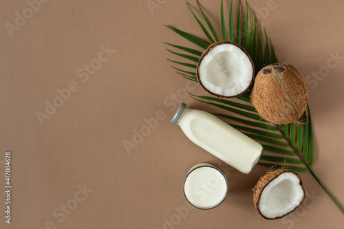 Coconut vegan milk with coconut halves top view on brown background.