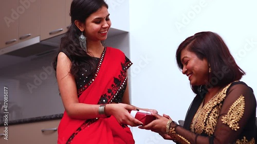 Cute young Indian woman wearing traditional ethnic clothes giving gift to a sister in living room home background happy new year or Diwali photo