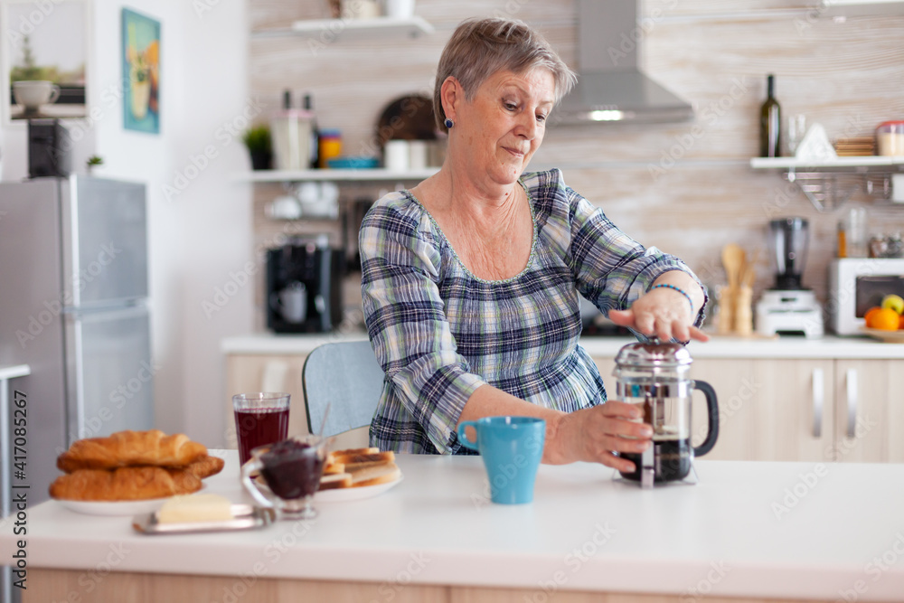 Happy senior woman pushing on french press while preparing coffee for breakfast. Elderly person in the morning enjoying fresh brown cafe espresso cup caffeine from vintage mug filter relax refreshment