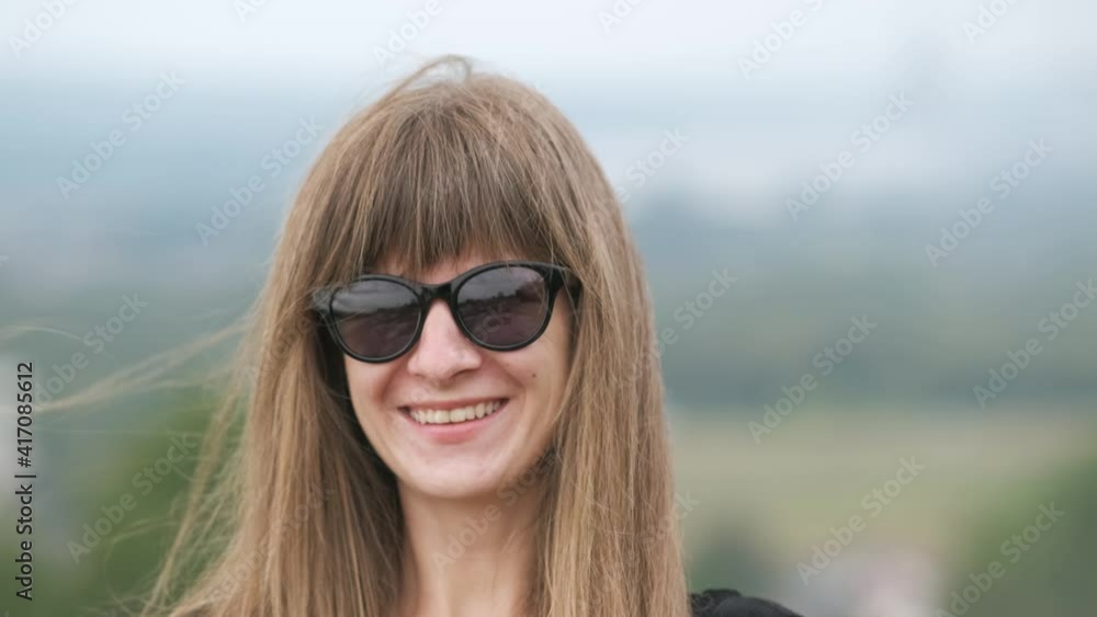 Portrait of a happy young long haired woman in dark sunglasses smiling in camera on a windy summer day. Portrait of a happy young long haired woman in dark sunglasses smiling in camera on a windy summer day.