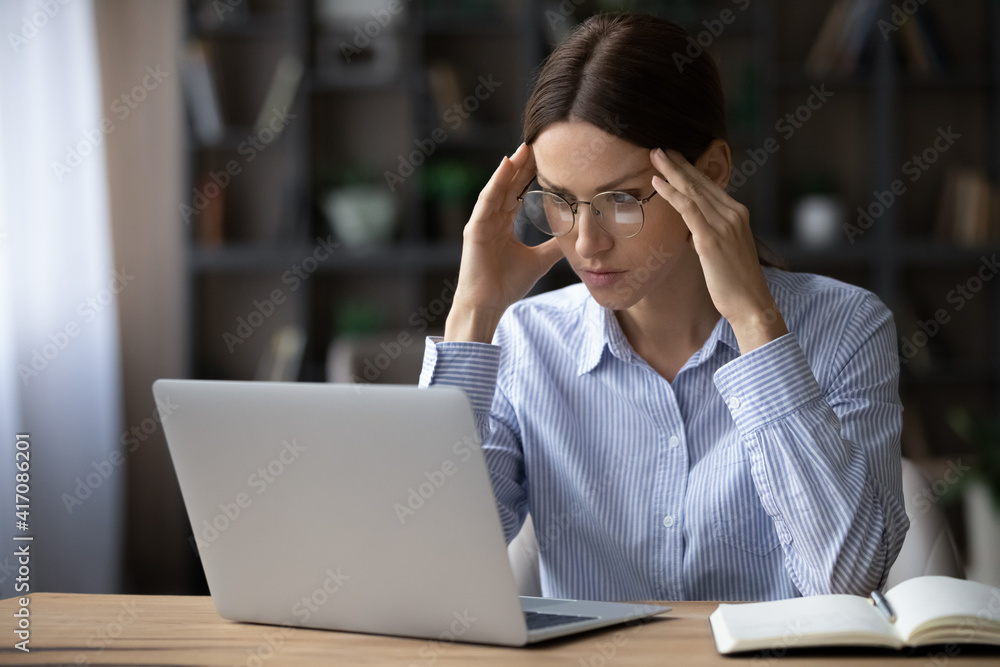 Unhappy young woman in glasses look at laptop screen feel distressed frustrated by gadget problem or scam. Mad angry businesswoman work on computer stressed with bad negative news online. Unhappy young woman in glasses look at laptop screen feel distressed frustrated by gadget problem or scam. Mad angry businesswoman work on computer stressed with bad negative news online.