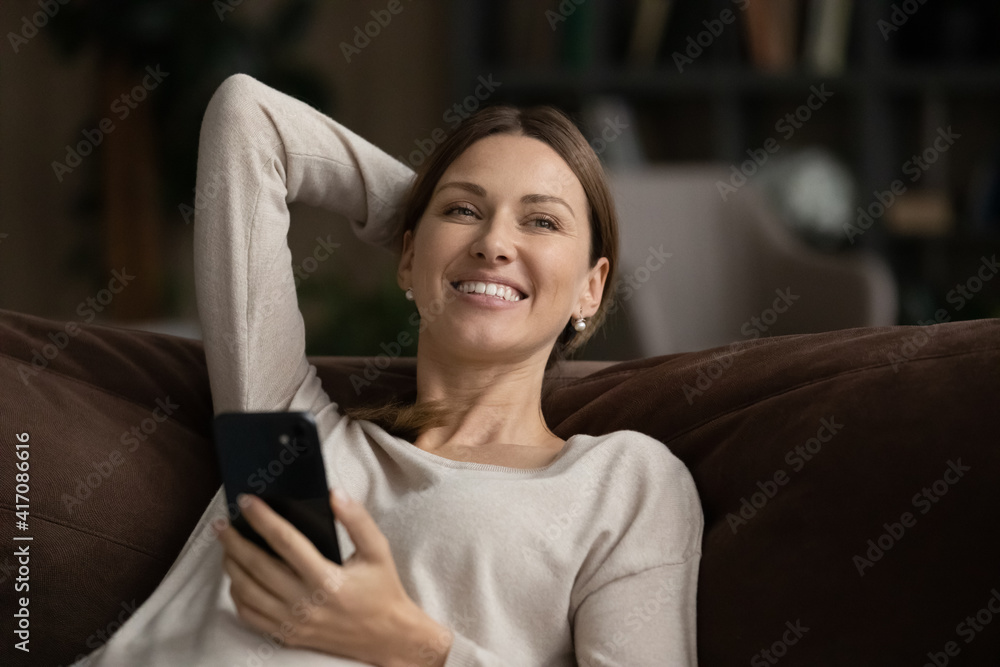 Smiling millennial Caucasian woman relax on couch at home use modern smartphone texting messaging online. Happy young female rest on sofa in living room browse internet on cellphone gadget. Smiling millennial Caucasian woman relax on couch at home use modern smartphone texting messaging online. Happy young female rest on sofa in living room browse internet on cellphone gadget.