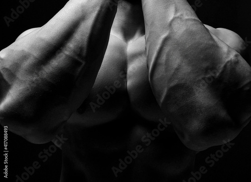 Closeup image of strong tight bodybuilder arms hands chest after fitness working out training. Black and white composition
