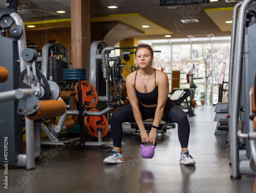 Smiling fit woman doing kettlebell swing in modern gym