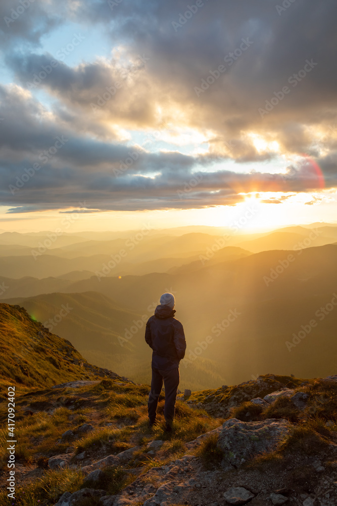 silhouette of the man at the top of the mountains peak looking at sunset