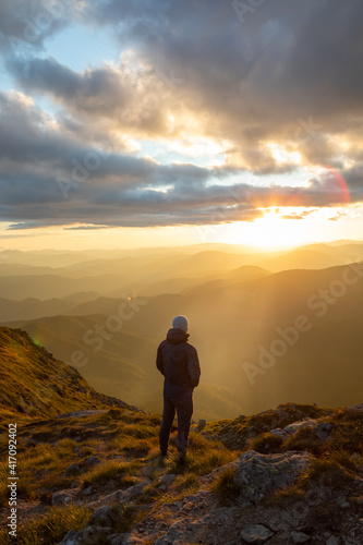 silhouette of the man at the top of the mountains peak looking at sunset