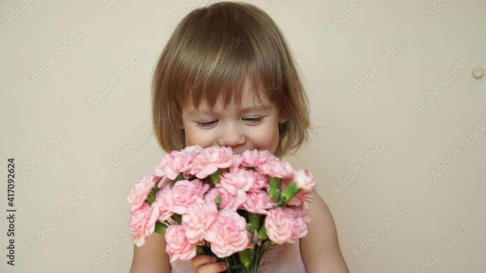 Portrait of little child girl holds bouquet of pink flowers, looks at camera, laughs, smiles and smells flowers. Spring, summer concept Portrait of little child girl holds bouquet of pink flowers, looks at camera, laughs, smiles and smells flowers. Spring, summer concept