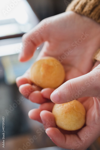 Hands holding pan de queijo, a Brazilian mini cheese bread finger food, party food and snack