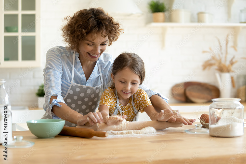 In four hands. Loving family of single mother small daughter child baking cake pastries cooking pie on dessert. Happy young mom bake sweet cookies with little kid roll dough at kitchen table using pin In four hands. Loving family of single mother small daughter child baking cake pastries cooking pie on dessert. Happy young mom bake sweet cookies with little kid roll dough at kitchen table using pin