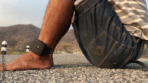 A male prisoner is attached to an Electronic Monitoring (EM) on his ankle. Standing on the road The prison was approved for release from the prison. By limiting the area to the area. photo