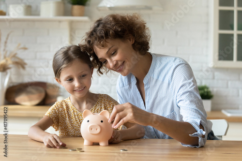 Setting good example. Young parent mother teach child little daughter girl to manage finances save money spend earnings with economy plan family budget. Friendly mom and kid thrift coins in piggybank photo