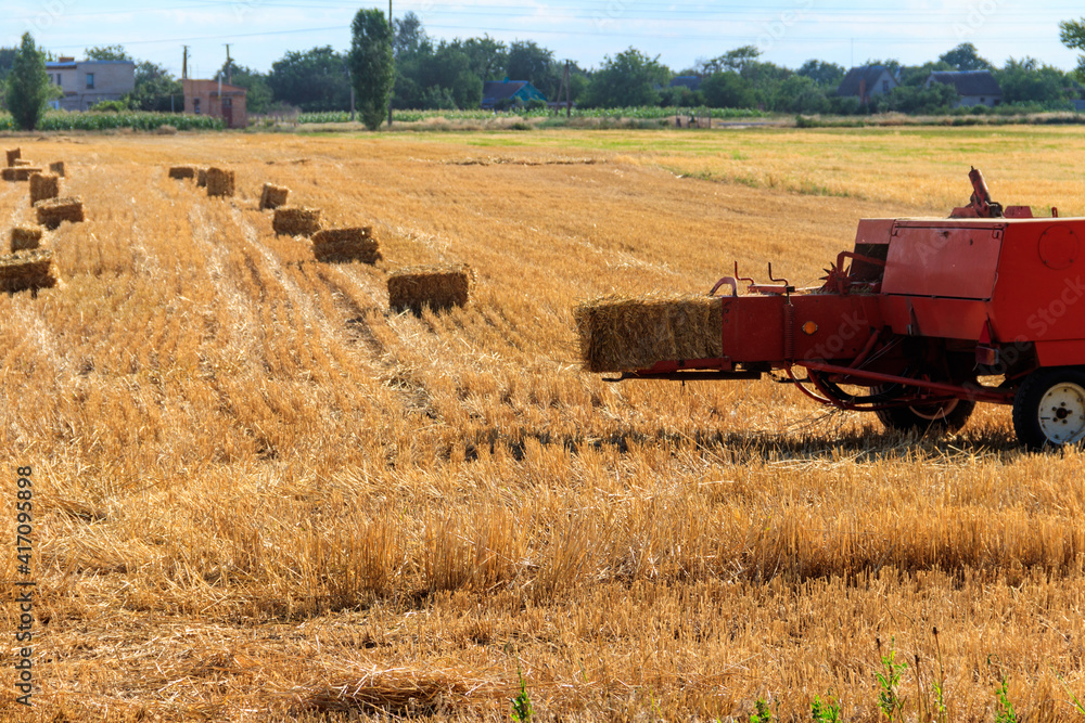 Fototapeta premium Rectangular baler discharges a straw bale in a field during the harvesting process