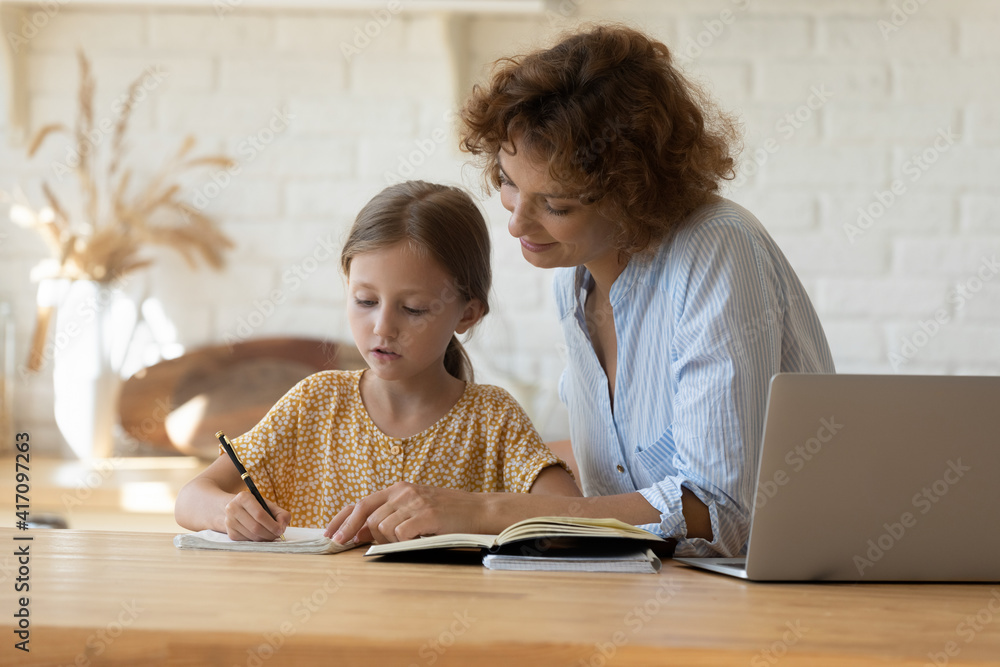 Private lesson. Attentive young woman tutor teacher help little girl pupil with studying math language correct mistakes explain learning material. Smiling mother assist small daughter with home task Private lesson. Attentive young woman tutor teacher help little girl pupil with studying math language correct mistakes explain learning material. Smiling mother assist small daughter with home task