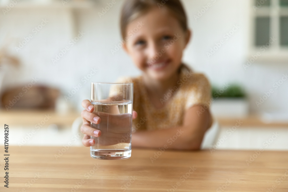 Taste this. Close up blurred portrait of small child girl looking at camera propose you drink clean purified cool natural mineral water to avoid dehydration. Focus on kid hand holding glass. Close up Taste this. Close up blurred portrait of small child girl looking at camera propose you drink clean purified cool natural mineral water to avoid dehydration. Focus on kid hand holding glass. Close up