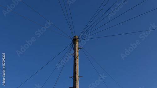 Wooden telegraph pole with wires leading off at angles against blue sky
