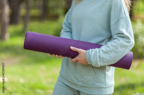 woman with yoga mat in her hands in the park at bright sunny day. Healthy lifestyle. Outdoor workout